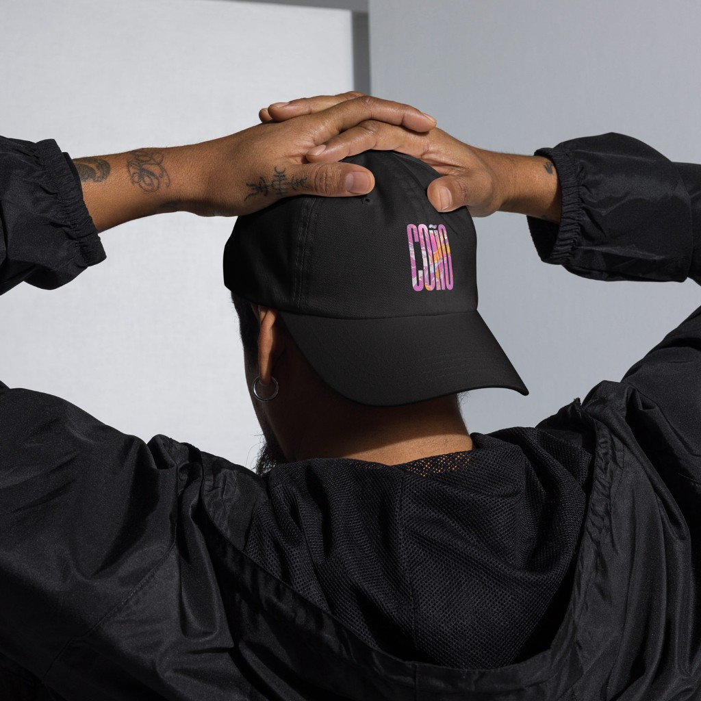 Model from behind in black Gayer Things Coño baseball cap — hands on crown, marble COÑO graphic