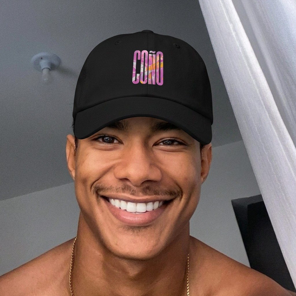 Lifestyle: shirtless model in black Gayer Things Coño cap against wood door — marble COÑO lettering
