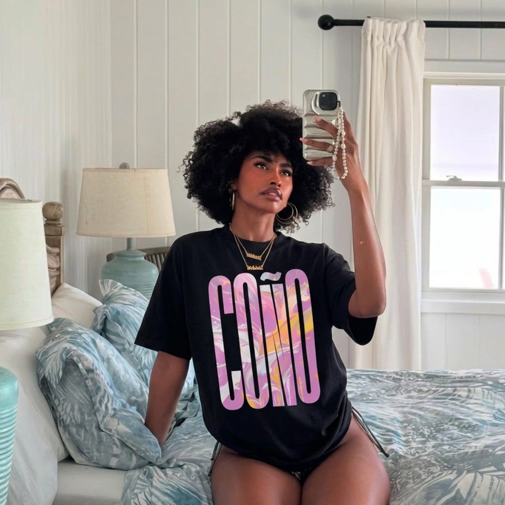 Mirror selfie: model in black Gayer Things Coño oversized organic tee — bedroom natural light, marble COÑO print